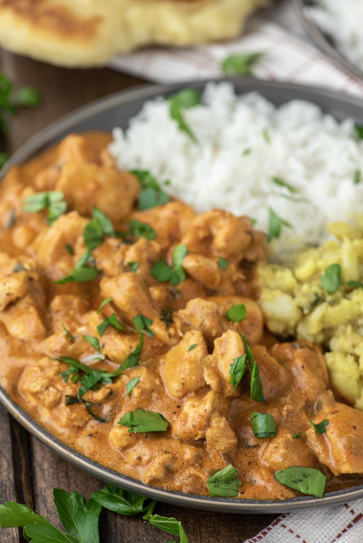 chicken masala on grey plate with aloo gobi and white rice