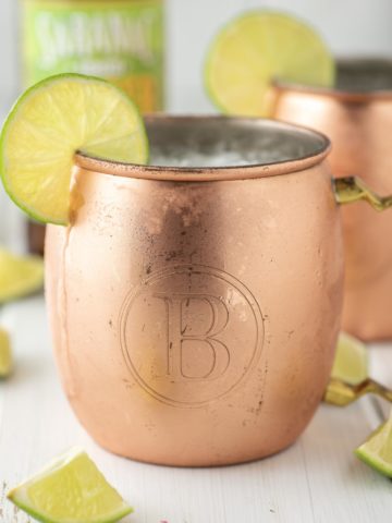 two moscow mules in copper mugs with ginger beer in background