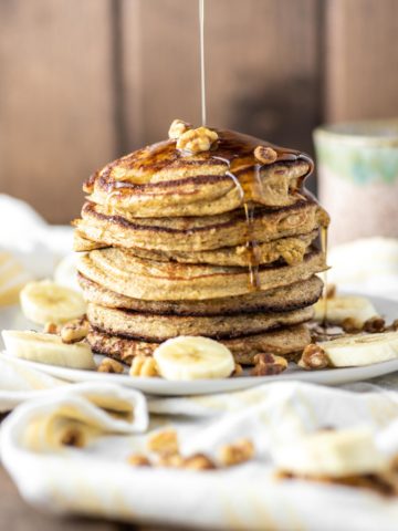 banana oat pancakes stacked on plate with maple syrup being drizzled on top