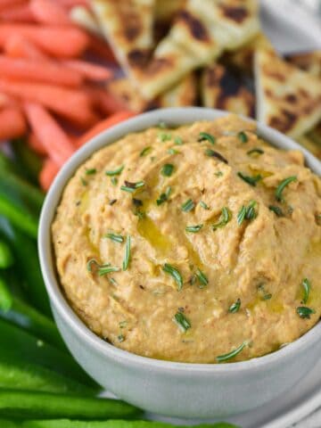 close-up of rosemary hummus in greenish grey ramekin with dipping options on plate