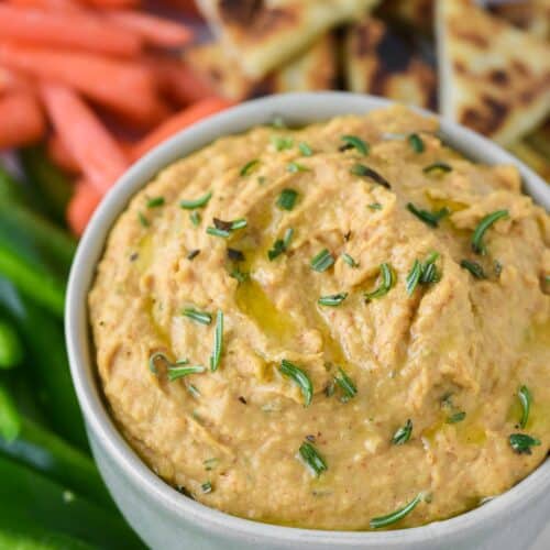 close-up of rosemary hummus in greenish grey ramekin with dipping options on plate