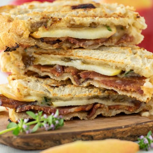 3 apple cheddar bacon paninis stacked on wood board