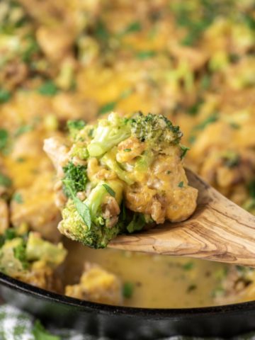 wooden spoon lifting out chicken, farro, broccoli and cheese from skillet