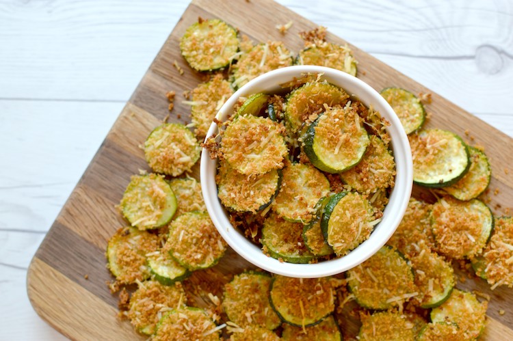 Overview of baked parmesan zucchini chips in small bowl on wood cutting board