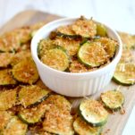 Baked parmesan zucchini chips in small bowl on wood cutting board