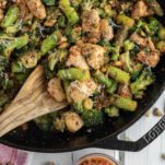 wooden spoon dipped in pesto chicken and veggies in cast iron skillet