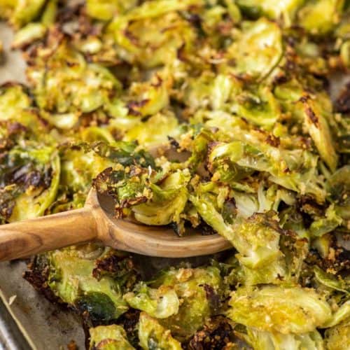 wooden spoon dipped in sheet pan of parmesan roasted Brussel sprouts