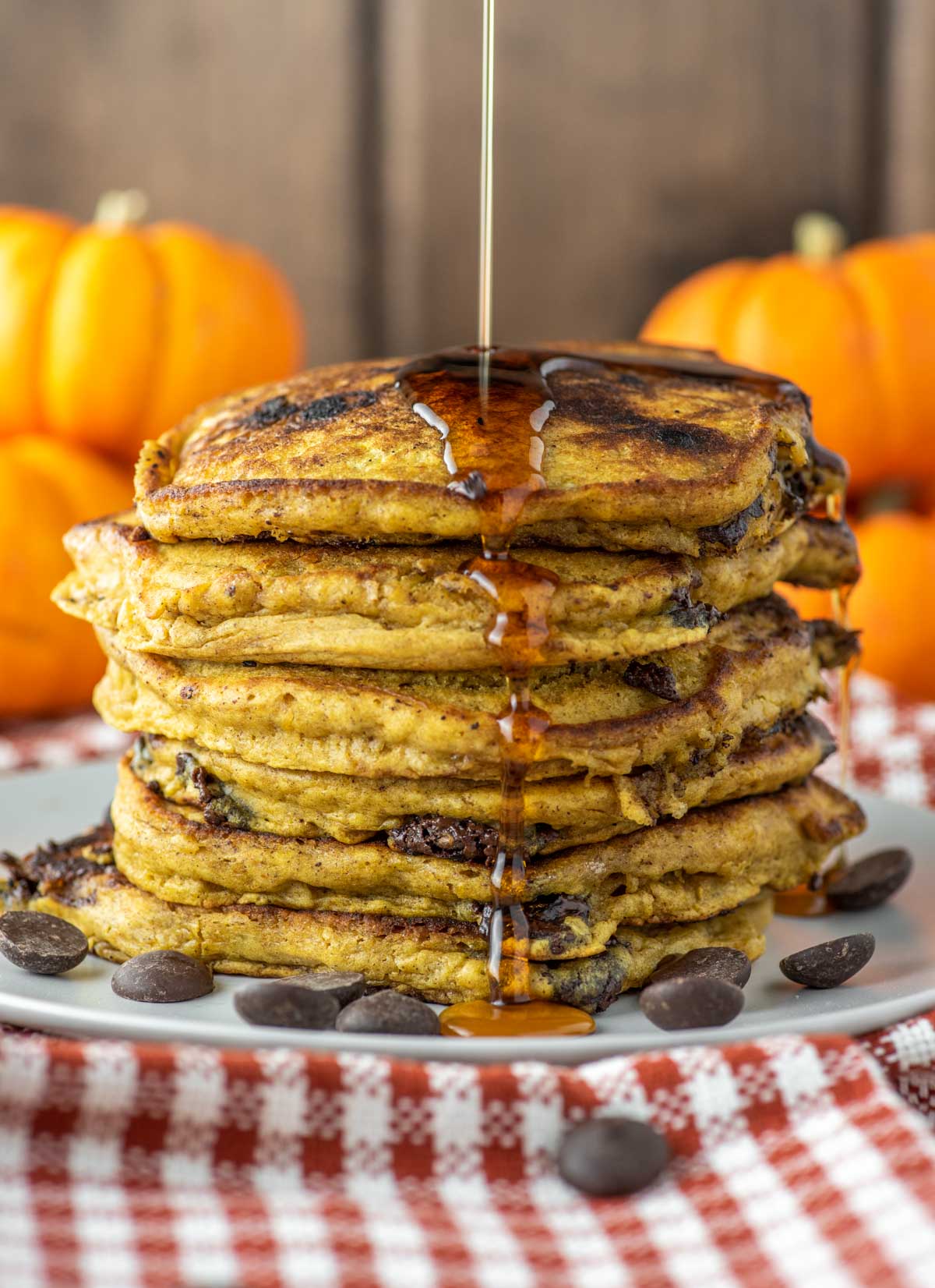 maple syrup being drizzled on stack of pumpkin chocolate chip pancakes