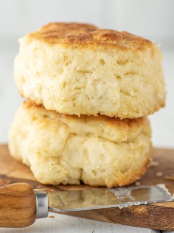 two buttermilk biscuits on wood board with butter knife