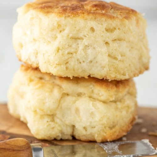 two buttermilk biscuits on wood board with butter knife