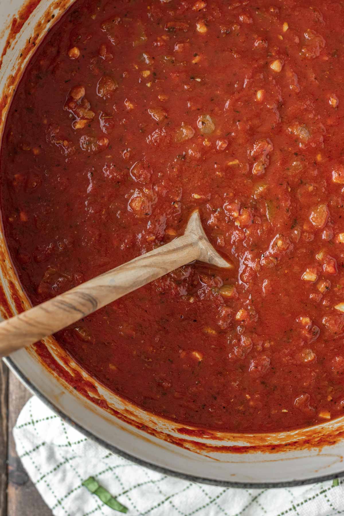 overhead shot of homemade marinara sauce in Dutch oven with wooden spoon dipped in it