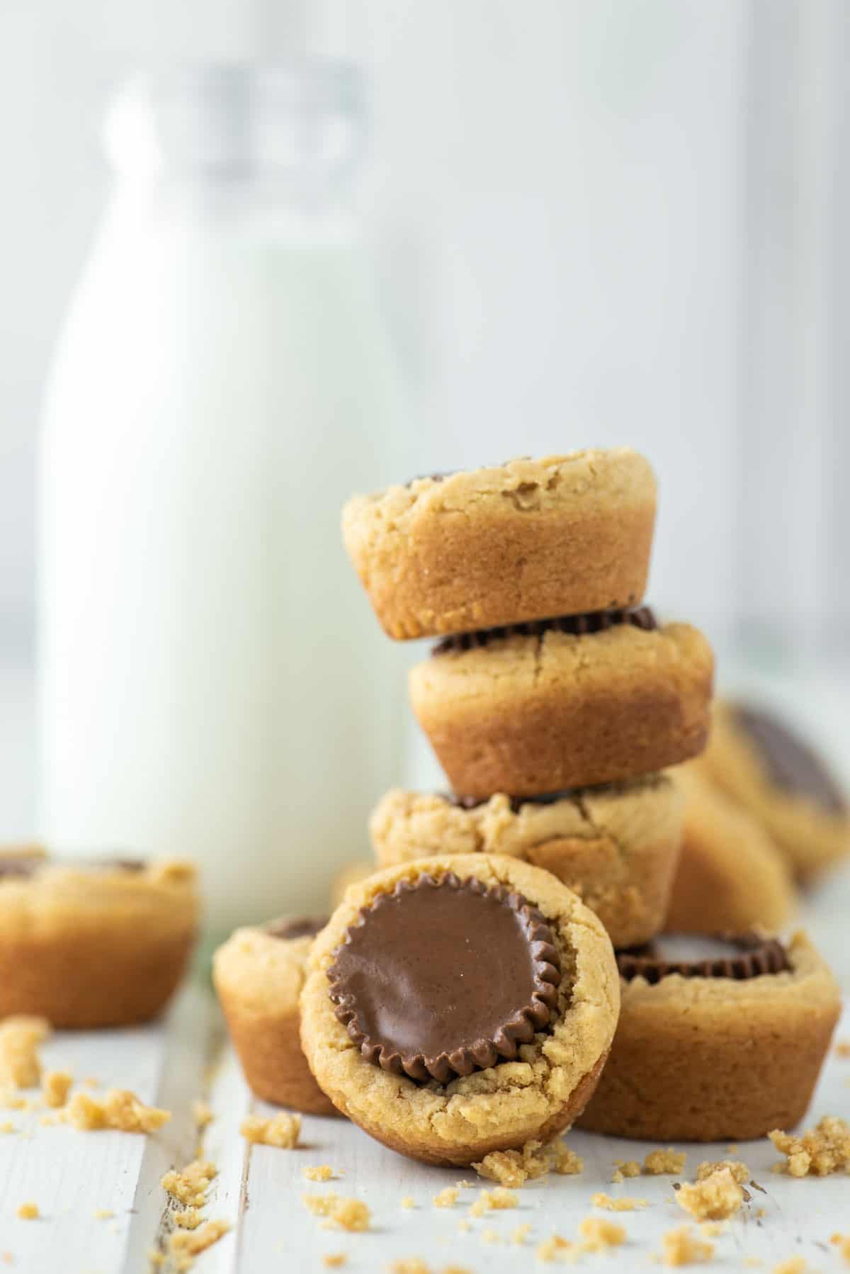 peanut butter cup cookies stacked on top of each other on white board with milk in background