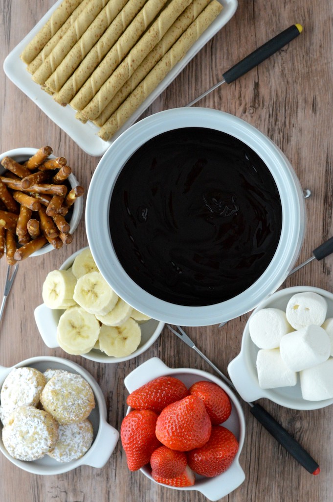 overhead shot of dark chocolate fondue in white pot with dippers around it