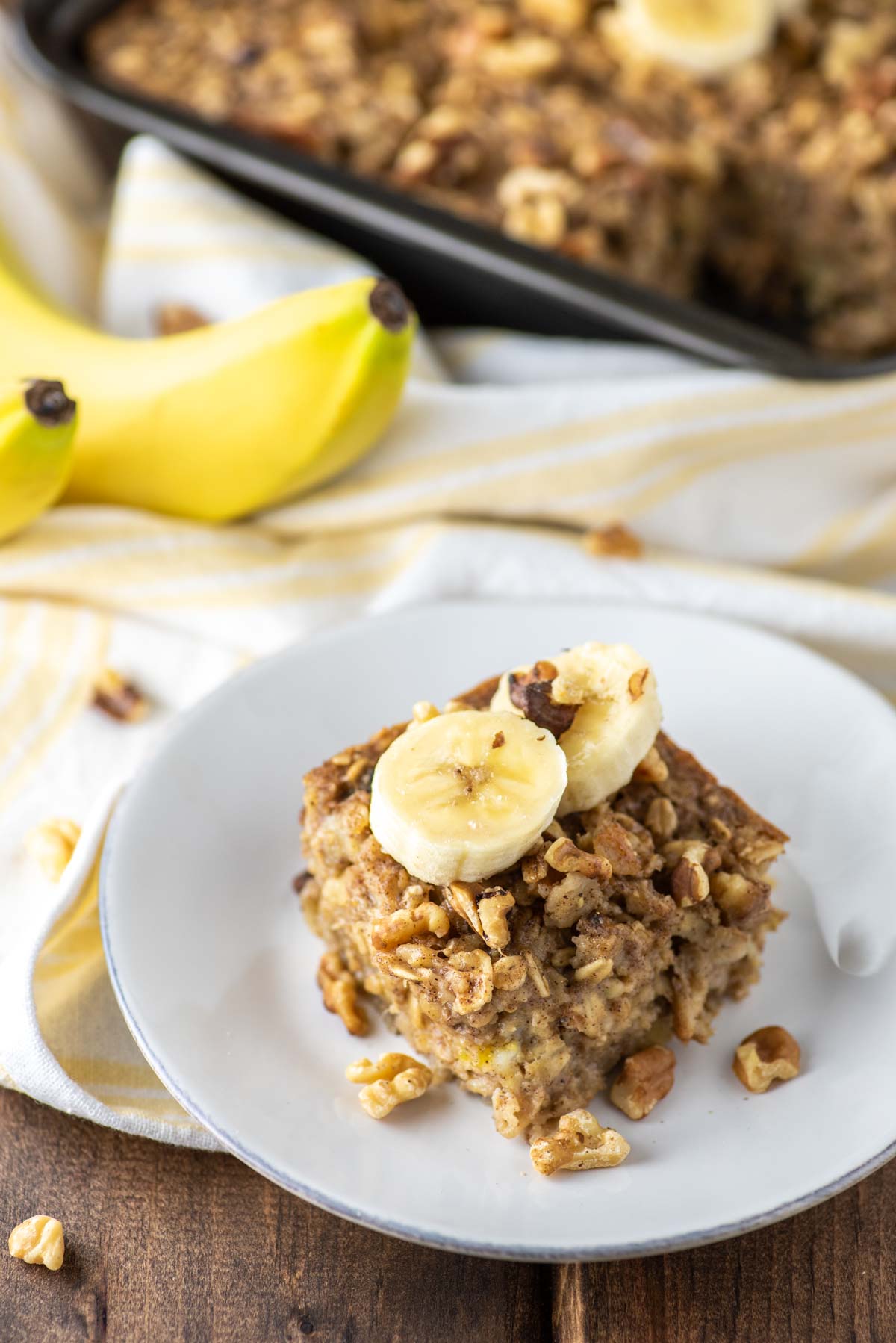 slice of banana baked oatmeal on white plate with pan in behind