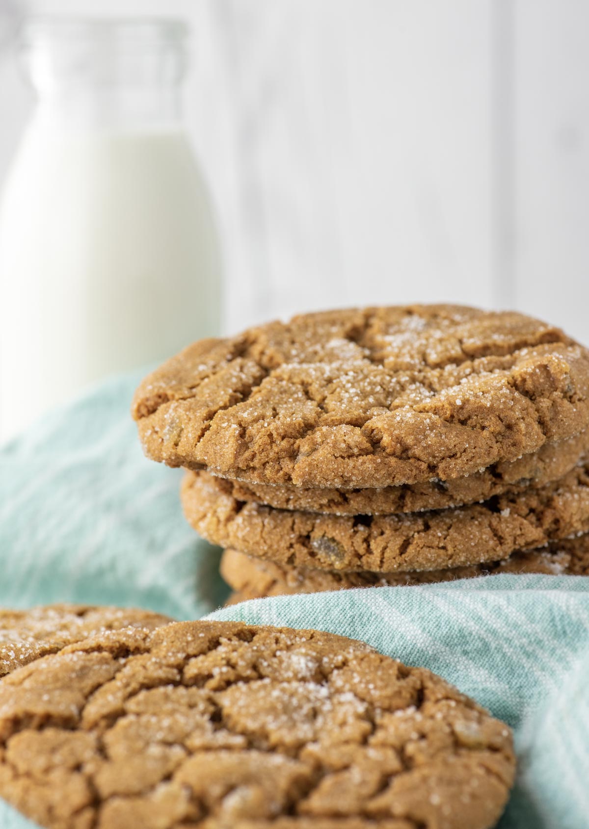 stacked ginger cookies on teal dish towel with glass of milk