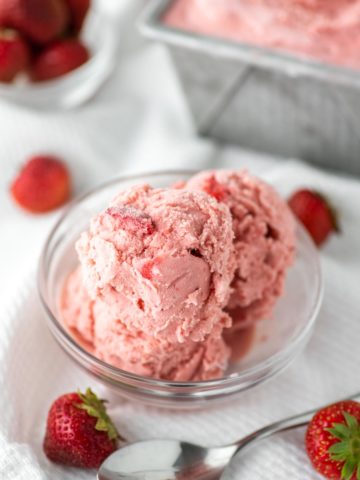 strawberry ice cream in glass bowl with container in background