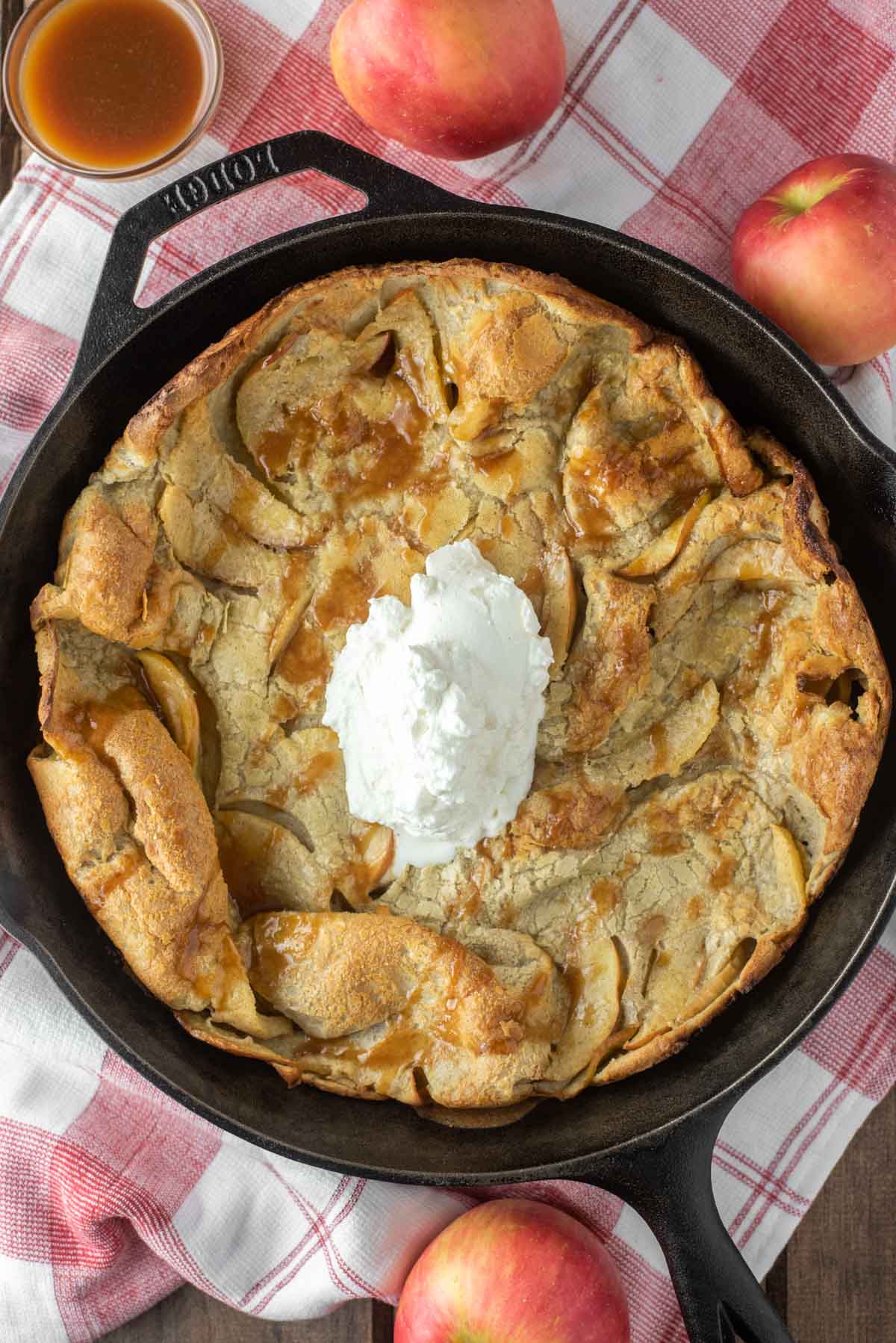 overhead shot of apple dutch baby with whipped cream in cast iron skillet