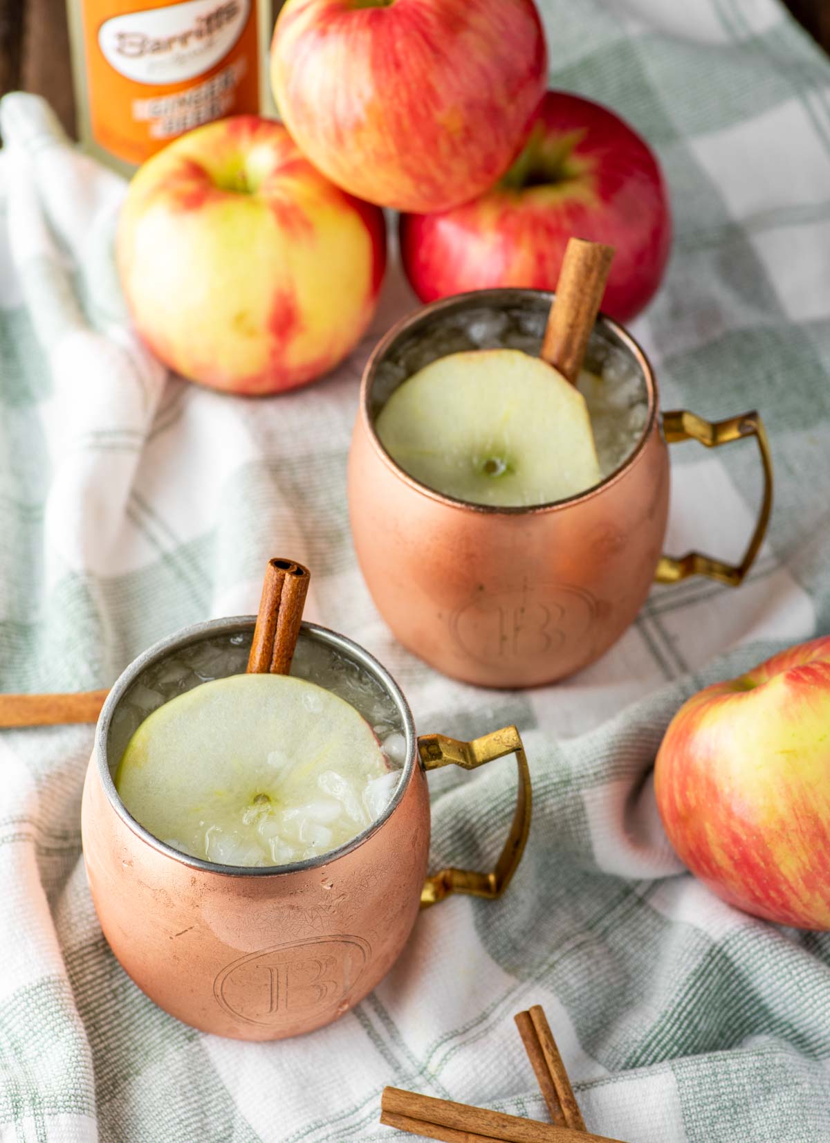two apple cider moscow mules in copper cups on dish towel