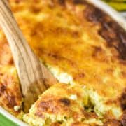 wooden spoon dipped in sweet corn pudding in green baking dish