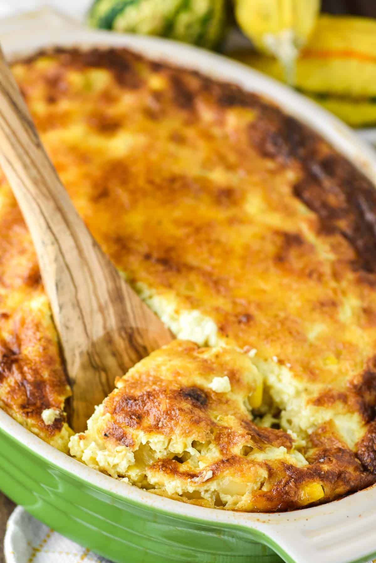 wooden spoon dipped in sweet corn pudding in green baking dish