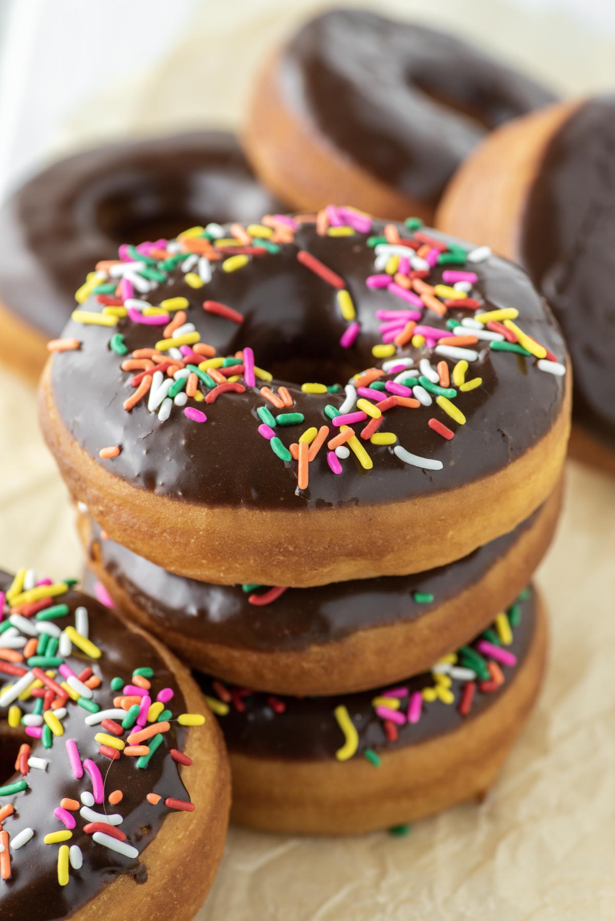 chocolate frosted donuts with sprinkles stacked on parchment paper