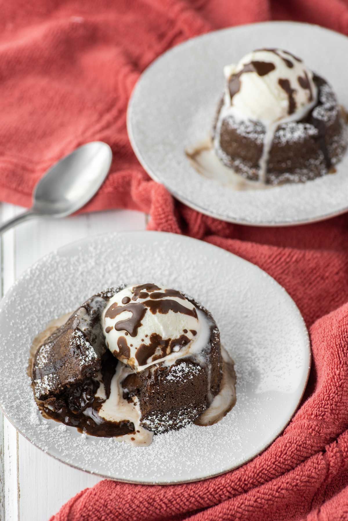 two lava cakes on white plates on red dish towel