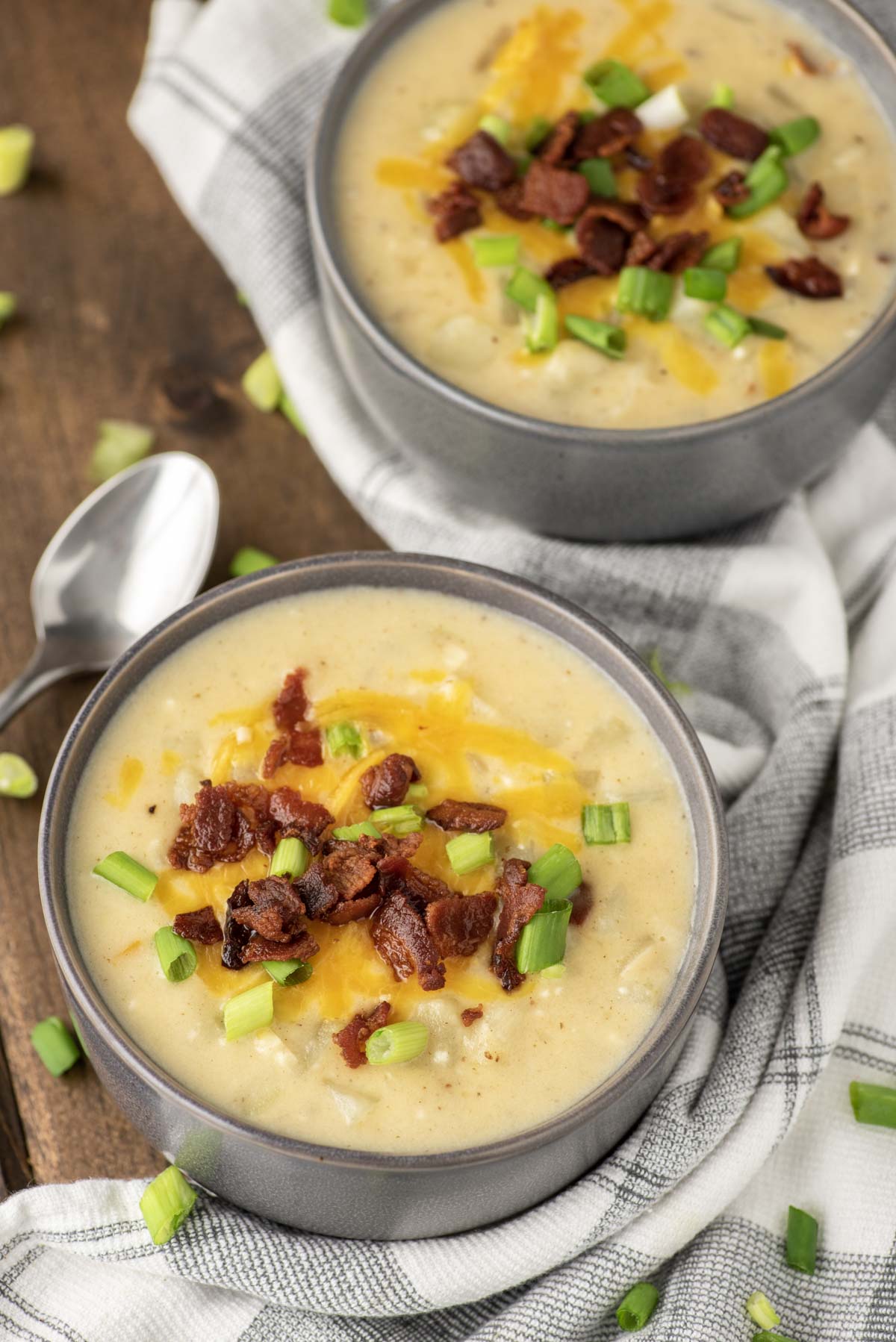 two grey bowls of potato soup topped with bacon and cheese