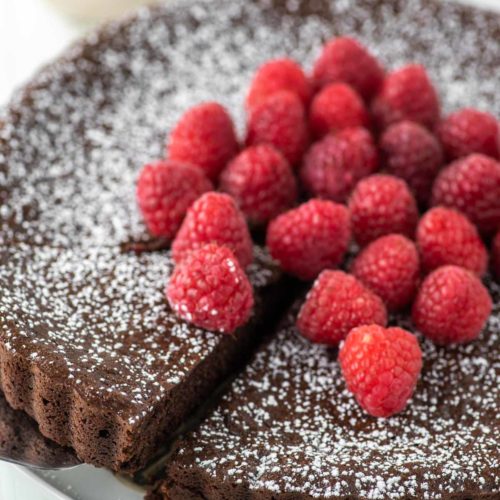 slice of flourless chocolate cake with raspberries being pulled away