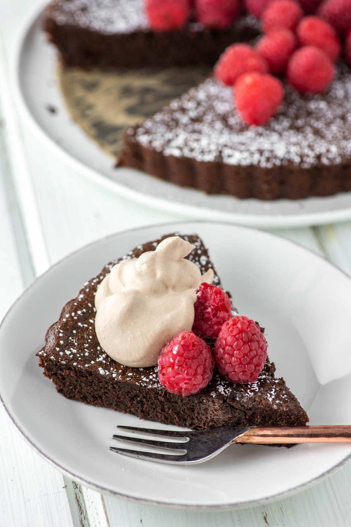 slice of flourless chocolate cake with raspberries and whipped cream on white plate