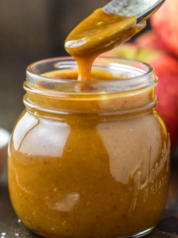 spoon lifting out apple cider caramel sauce from jar