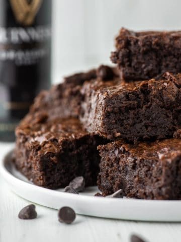 Guinness brownies stacked on white plate with beer bottle in background
