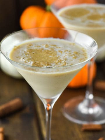 two glasses of pumpkin spice martinis with pumpkins in the background