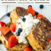 3 stacked slices of French toast on plate with whipped cream and fruit