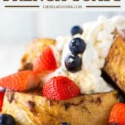 sourdough French toast stacked on white plate with whipped cream and fruit