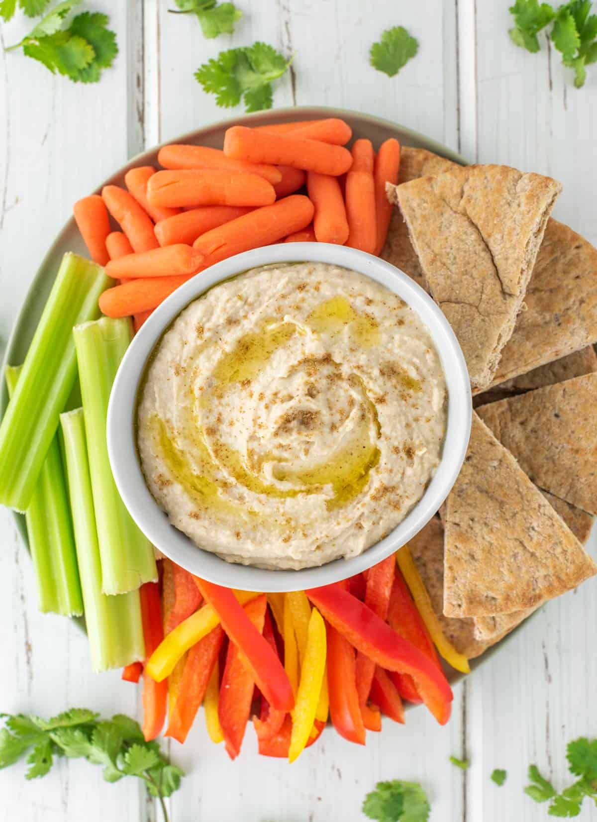 overhead shot of bowl of white bean hummus on plate with carrots, pita bread, peppers and celery