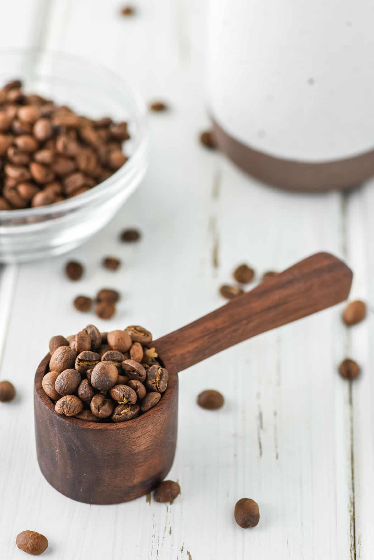 wooden coffee scoop with coffee beans on white board and coffee mug in background