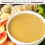 white bowl of cheddar cheese fondue with plate of veggies, fruit and bread