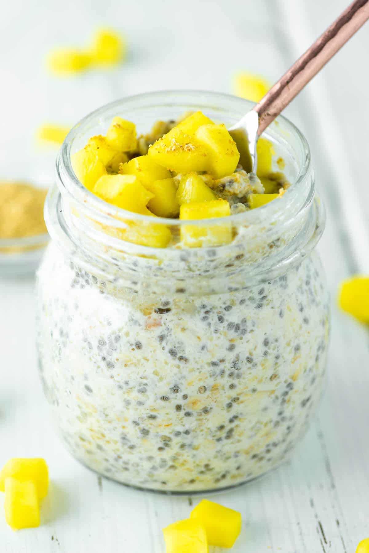 spoon dipped in glass jar of mango overnight oats