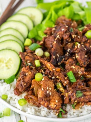spicy pork bulgogi on white plate of rice with cucumbers and lettuce