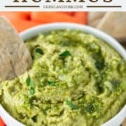 pita bread dipping in white bowl of hummus with pesto