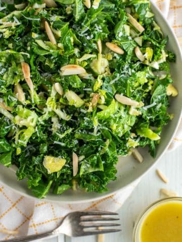 overhead shot of kale crunch salad on plate with fork to the side and bowl of vinaigrette