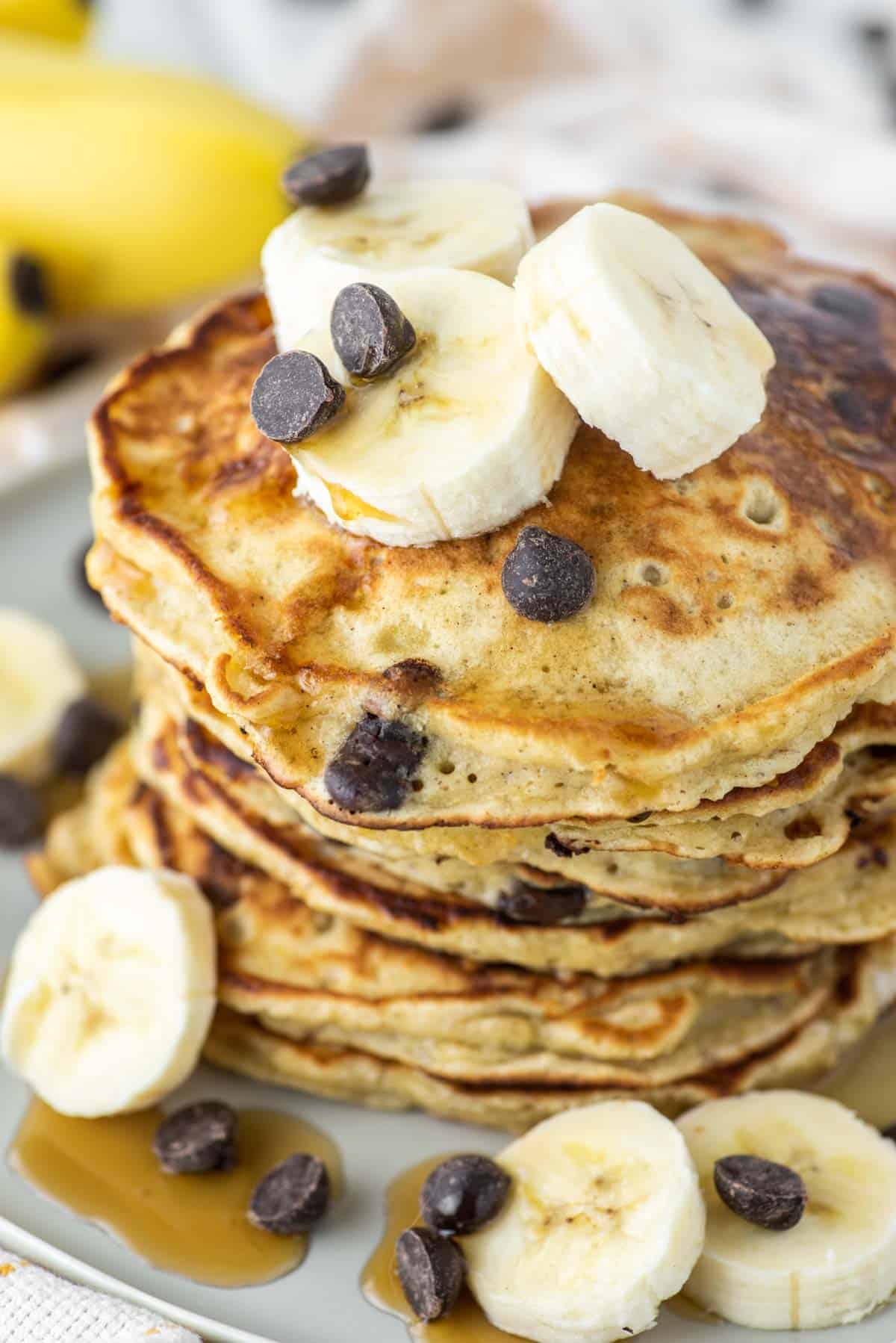 banana chocolate chip pancakes stacked on plate with bananas on top