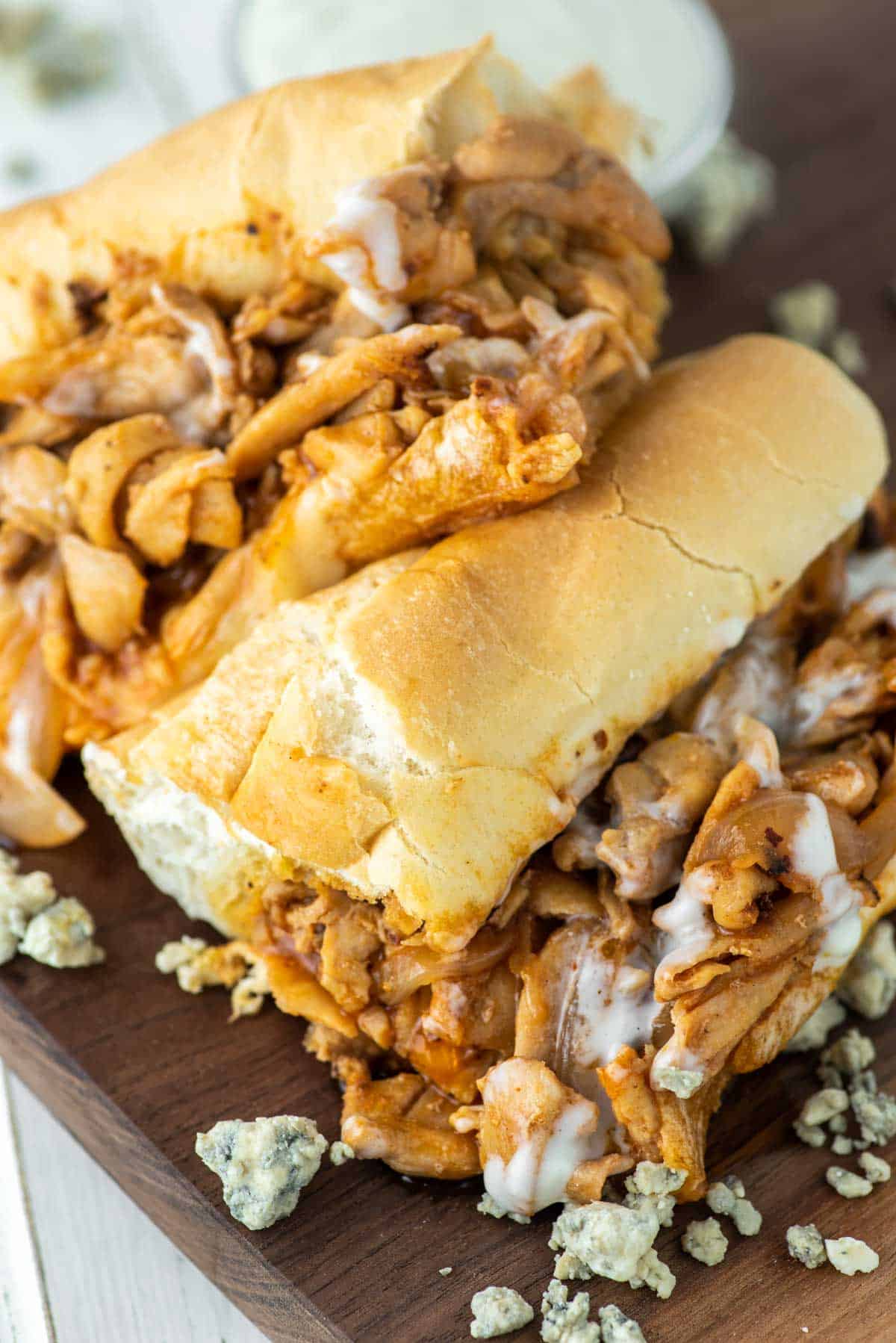 buffalo chicken cheesesteak cut in half and stacked on top of each on wood board