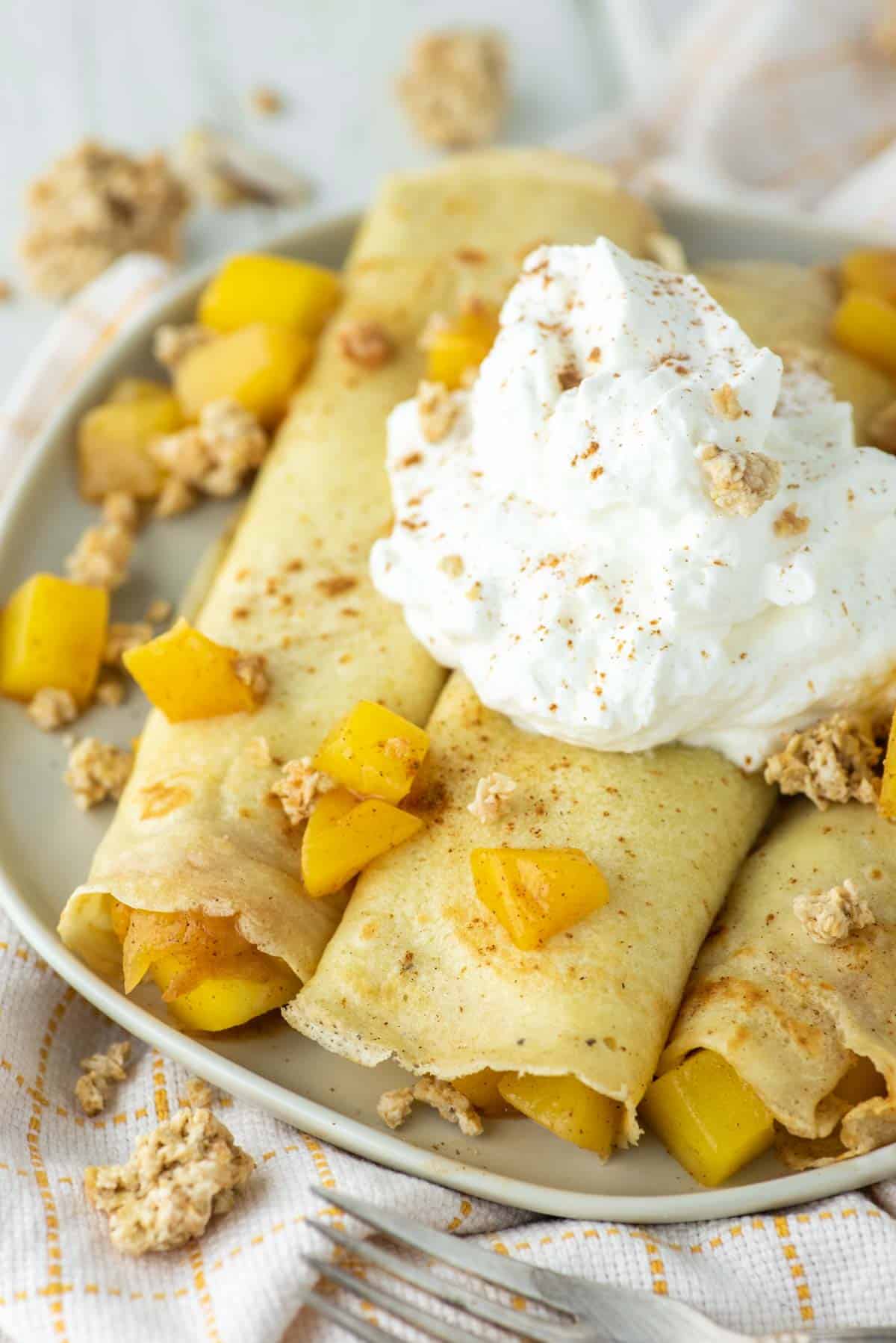 3 mango crepes rolled up on plate with whipped cream on top