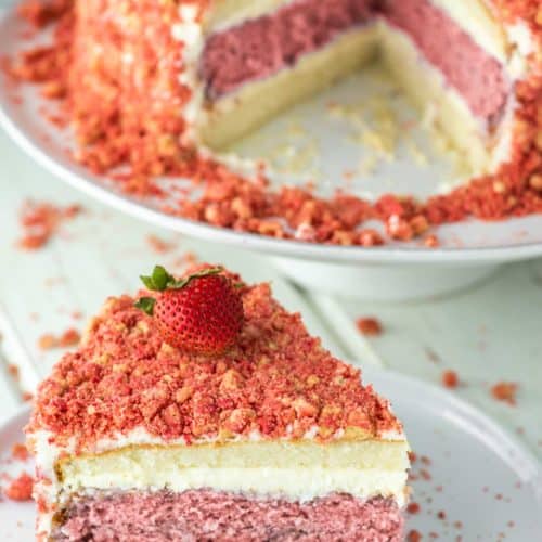 slice of strawberry crunch cake on white plate with rest of cake on cake stand