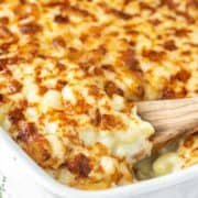wooden spoon lifting out white cheddar mac and cheese from white baking dish