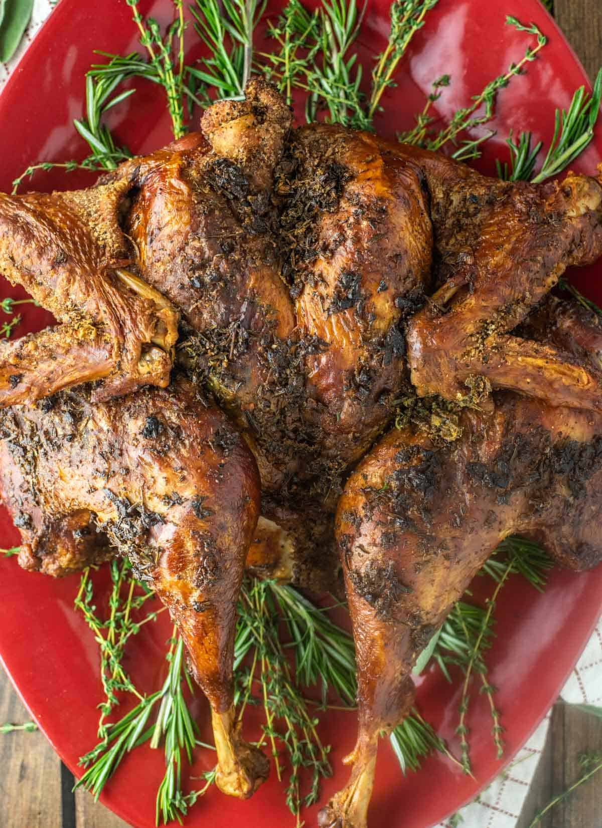 overhead shot of spatchcock smoked turkey on red plate with herbs