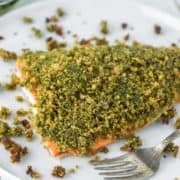 salmon topped with a pesto breadcrumb mixture on white plate with fork