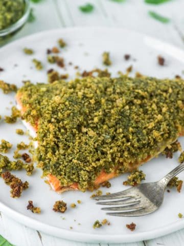 salmon topped with a pesto breadcrumb mixture on white plate with fork