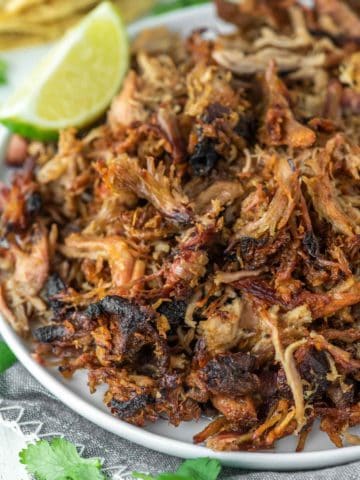 close-up shot of smoked carnitas on white plate with lime wedge